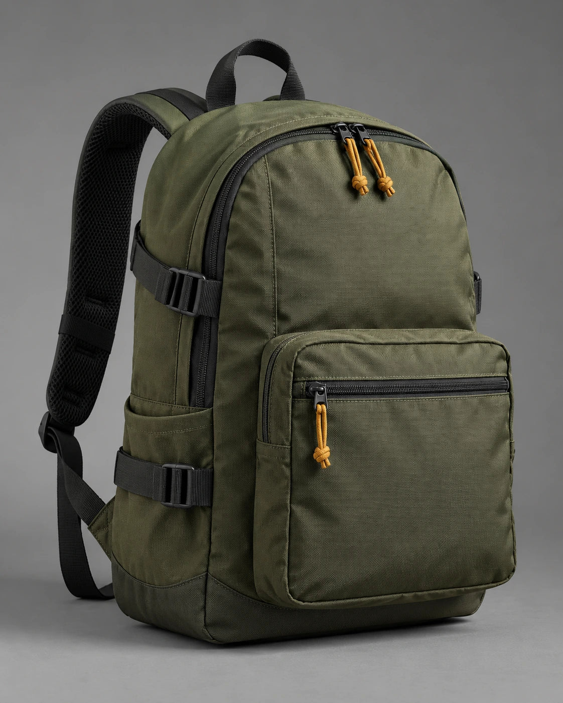 Olive utility backpack with a front pocket, black webbing and ochre zip pulls on a grey background.