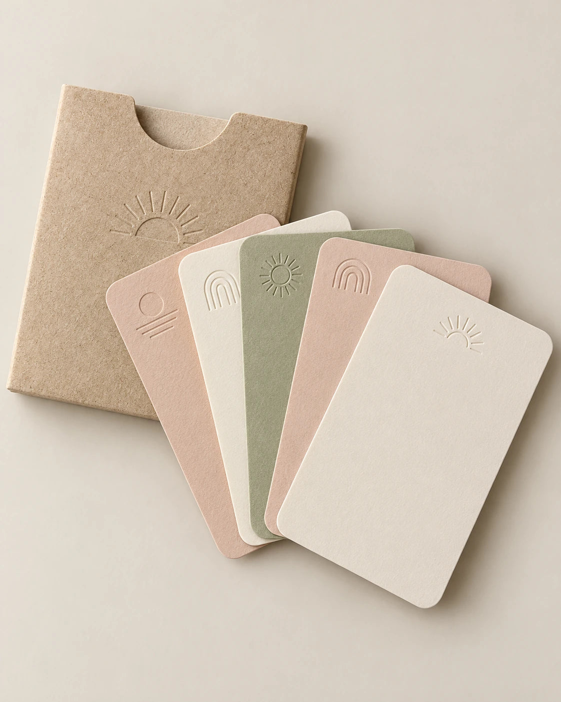 Cream, blush and sage keepsake cards with small embossed sun and arch motifs, arranged beside a paper sleeve.