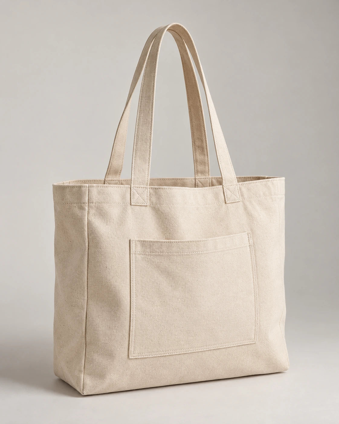 Natural canvas tote bag with long handles and a stitched exterior pocket on a pale background.